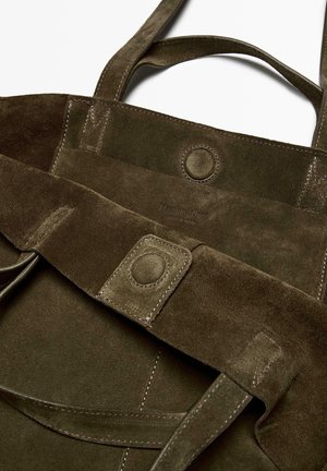Olivgrüne Wildleder-Shopper-Tasche mit zwei Schulterriemen, ausgestattet mit einem Druckverschluss und einem geprägten Logo. Sanfte Textur mit sichtbaren Nähdetails.