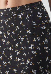 Falda de tela negra con un patrón floral que presenta flores blancas, acentos amarillos y morados. Textura suave, cintura elástica, diseño casual.