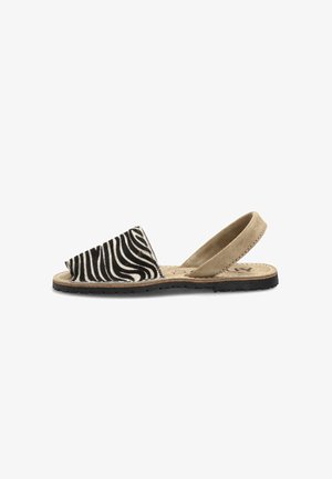 Sandalia plana con tira frontal de estampado de cebra en blanco y negro y tira trasera de ante beige sobre suela de goma.