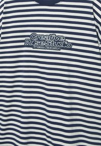 Navy and white horizontal striped shirt with "Creative Pulse Studio Timeless Dedication" embroidered in navy on the chest.