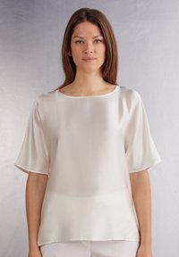 Blusa de color crema, de manga corta, hecha de un tejido ligero y suave. Presenta un escote redondeado y un diseño minimalista y limpio.