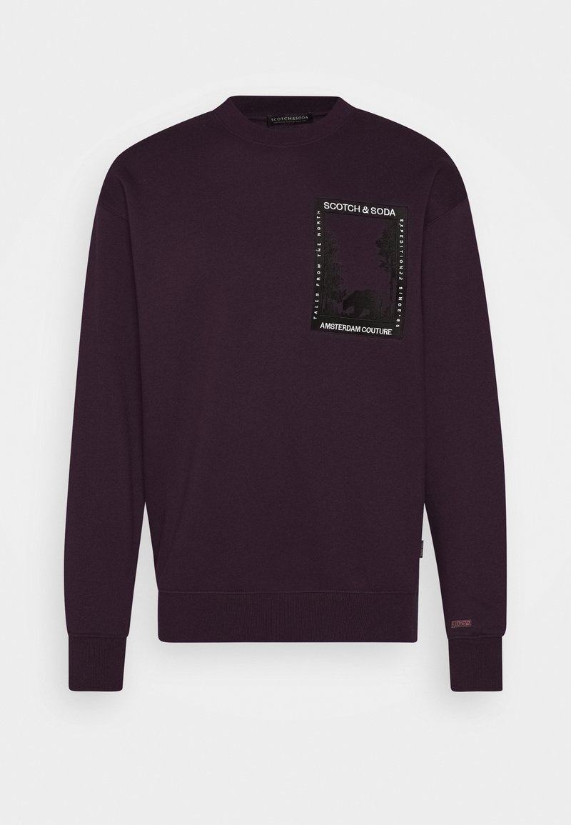 Donkerpaarse sweatshirt met ronde hals, geribbelde boorden en zoom, met een rechthoekige patch met "Scotch & Soda" en een abstracte natuurafbeelding op de borst.