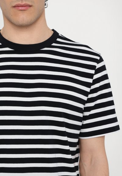 Camiseta a rayas en blanco y negro, de manga corta, con cuello redondo, material de algodón suave y rayas horizontales uniformemente espaciadas.