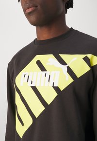 Felpa nera con grande design grafico in neon giallo, che include il logo "PUMA" e forme stilizzate, realizzata in tessuto texturizzato.
