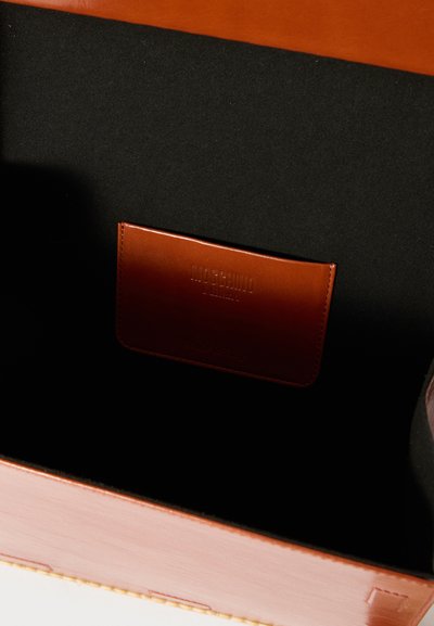 Brun læder håndtaske med en glat overflade, der har en sort indvendig og en lille, prægede lomme med mærkningen "Moschino."