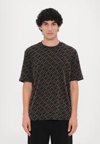 Tricou negru cu mânecă scurtă, având un model geometric în nuanțe de bej, guler rotund, croi lejer și textură moale. Design minimalist.