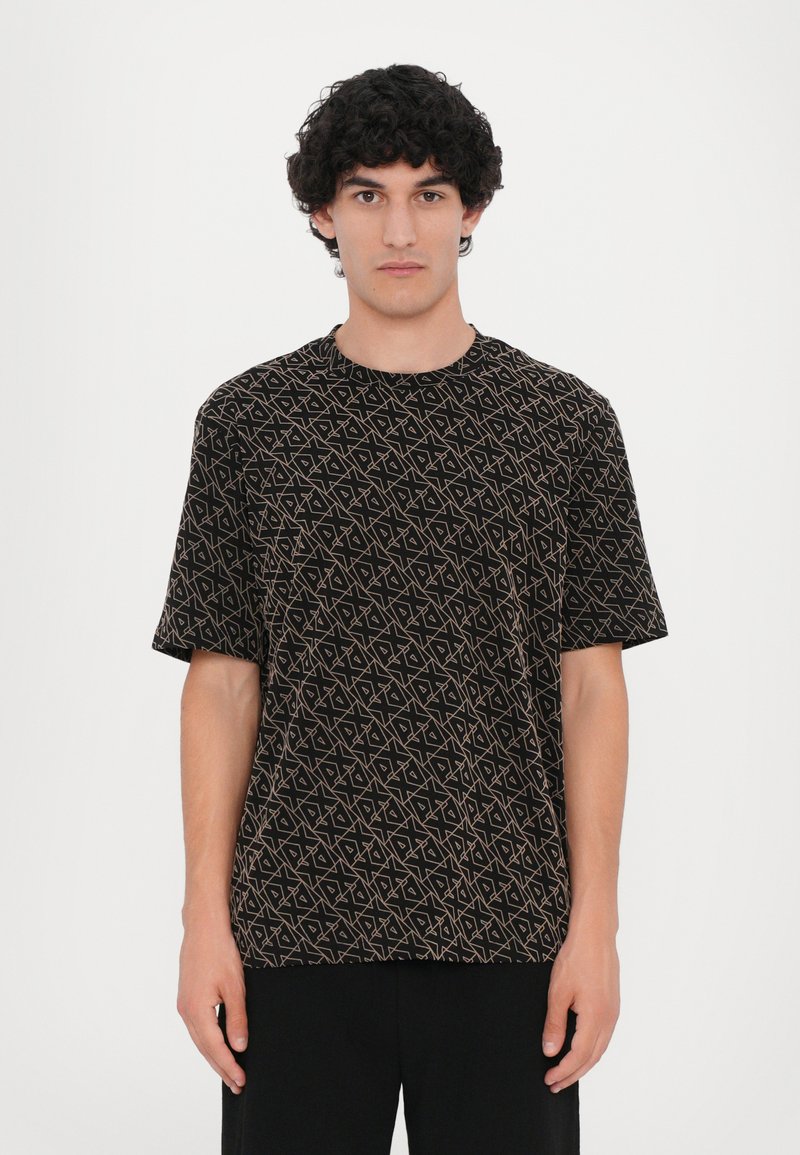 Tricou negru cu mânecă scurtă, având un model geometric în nuanțe de bej, guler rotund, croi lejer și textură moale. Design minimalist.