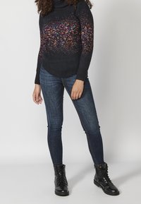 Černý pletený svetr s rolákem a vícebarevnými tečkami na hrudi; v kombinaci s tmavě modrými skinny jeans a černými šněrovacími botami.