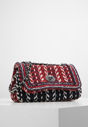 Kleine handtas met rood, wit en marineblauw geweven patroon, zilveren draaisluiting en zilveren kettingbandje, geplaatst op een witte ondergrond en achtergrond.