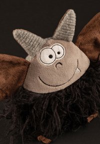 Plush toy with a round face, large eyes, gray fabric horns, brown fabric ears, and a black shaggy body. Features a stitched smile and small fangs.