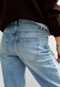 Jeans de mezclilla azul claro con cintura alta, que cuentan con grandes bolsillos traseros y costuras visibles. Textura suave y corte relajado.