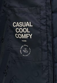 Navyblauer Pufferjackenstoff mit glatter Textur. Verfügt über eine aufgenähte Tasche mit weißem Text "CASUAL COOL COMFY" und einem Pflegeetikett-Grafik.