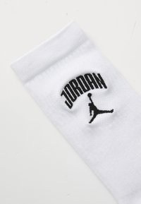 Calcetín blanco de algodón con puño acanalado que presenta un logo "JORDAN" en negro y la icónica silueta Jumpman bordada en negro.