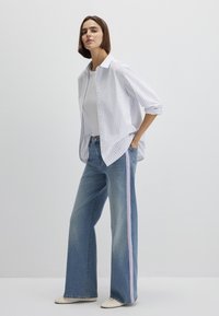 Striped button-up shirt in white and blue, paired with wide-leg blue jeans featuring pink side stripes. Fabric appears lightweight.