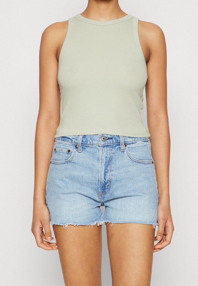 Světl zelený pletený top s kulatým výstřihem, v kombinaci s vysokými modrými džínovými šortkami se třepeným lemem.
