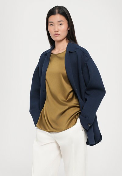 Tumesinine üleöö jakki, kuldne satiintop ja valged püksid. Siledad tekstuurid, pehme kangas ja mugav siluett minimaalse detailihulgaga.