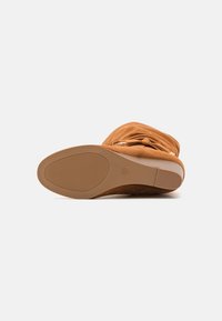 Stivaletto alla caviglia in suede marrone con un design morbido. Presenta una suola in gomma piatta con una presa texturizzata e un delicato dettaglio di cucitura.