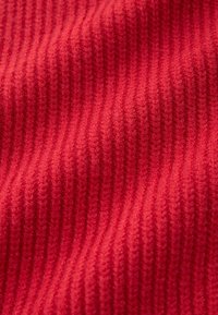 Tkanina tekstylna w jasnoczerwonym kolorze o prążkowanej fakturze. Miękka i lekko puszysta powierzchnia. Wzór składa się z pionowych linii.