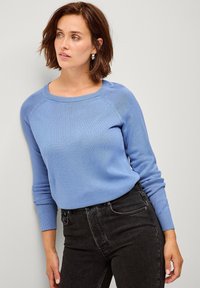 Lichtblauwe gebreide trui met een ronde halslijn en geribbelde boorden, gecombineerd met donkergrijze jeans. Soepele textuur en aansluitend ontwerp.