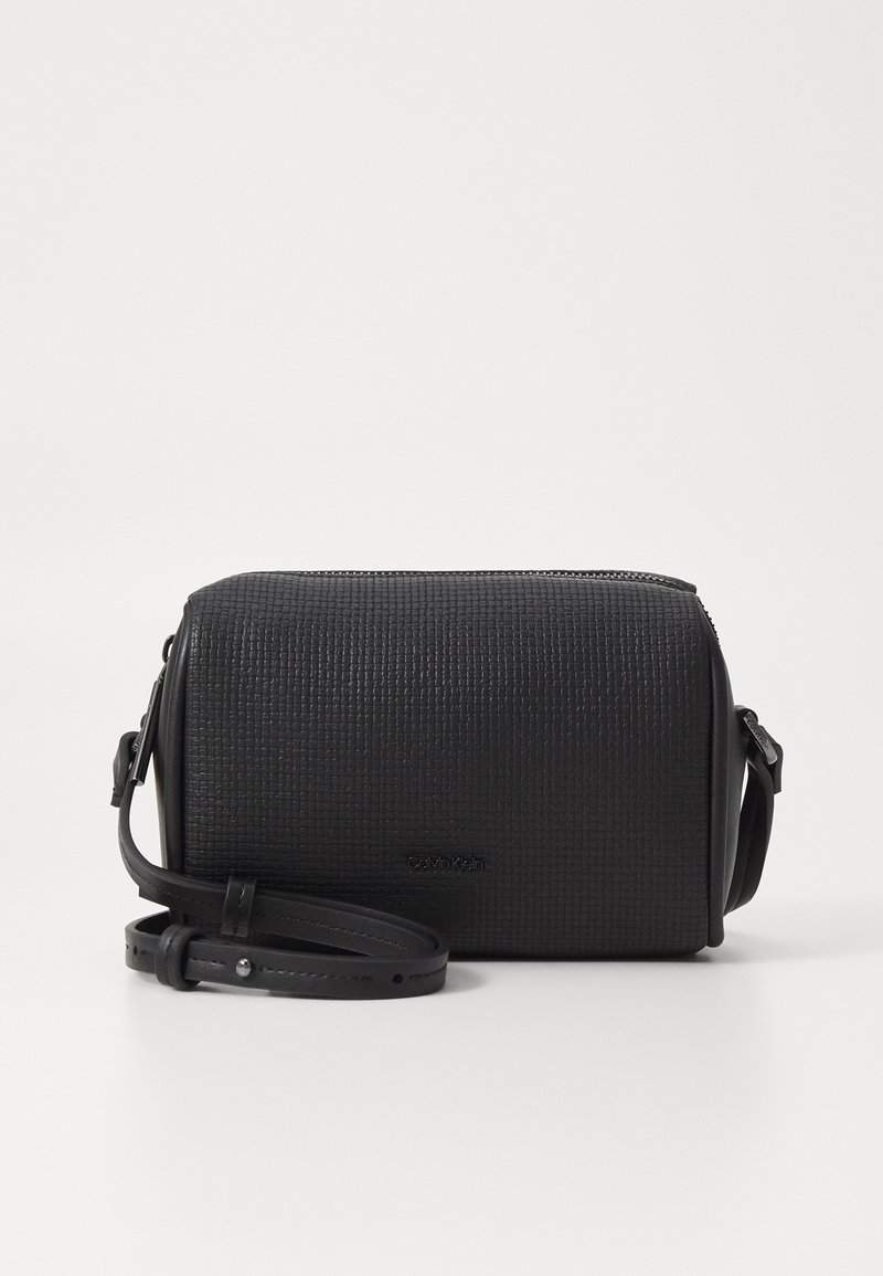 Black textured crossbody bag with a flat rectangular shape, featuring a zip closure and an adjustable strap. Logo embossed on the front.