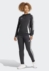 Haut de sport noir à capuche et leggings avec des rayures blanches sur les côtés. Fabriqué en tissu lisse et extensible. Doté d'une capuche à cordon de serrage et d'accents de logo.