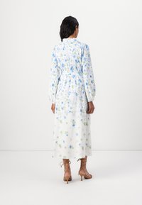 Vestido maxi floral em tecido leve, com padrões florais azuis e verdes, mangas longas bufantes e cintura ajustada nas costas.