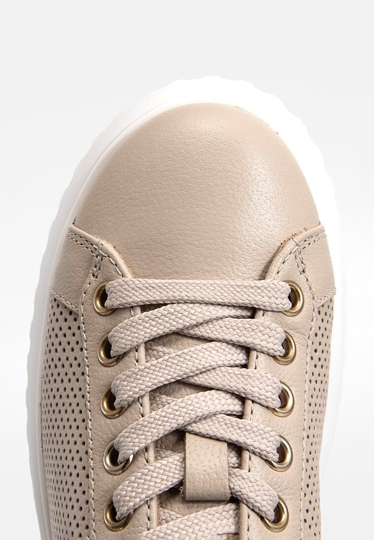 Jasno beżowy sneaker z gładkiej skóry, z perforowanymi detalami, okrągłym noskiem, złotymi oczkami i płaskimi plecionymi sznurowadłami na białej podeszwie.