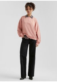 Sudadera de gran tamaño en color rosa pastel con puños acanalados, superpuesta a una camisa de cuello con estampado de cebra en blanco y negro, combinada con pantalones de pierna ancha negros.