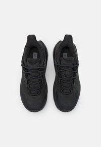 Zapatillas negras con una combinación de tejido texturizado y superposiciones suaves, que presentan un diseño de cordones y un collar acolchado para mayor comodidad.