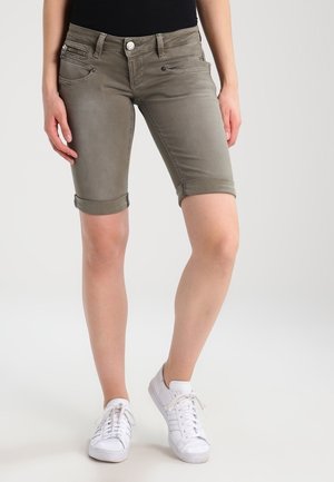 Bermudas de denim caqui con puños enrollados, con bolsillos frontales y detalles de costura sutil, combinadas con zapatillas blancas.