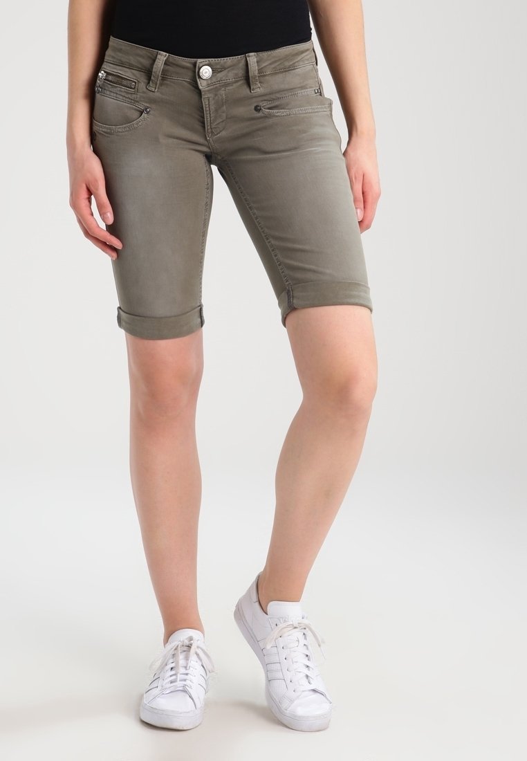 Bermudas de denim caqui con puños enrollados, con bolsillos frontales y detalles de costura sutil, combinadas con zapatillas blancas.