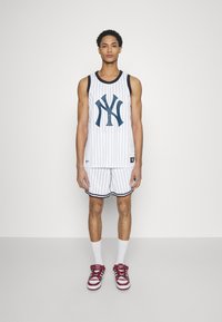 Canotta e pantaloni corti da basket a righe bianche con un logo blu navy, abbinati a scarpe da ginnastica rosse e calze bianche alla caviglia.