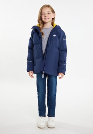 Marineblå polstret jakke med lynlås og gul hættefor. Har elastiske manchetter og brændmærker. Båret over en grå top og jeans.
