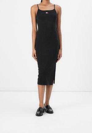 Robe noire mi-longue avec fines bretelles, dotée d'une fente sur le côté et d'un petit logo multicolore sur la poitrine. Tissu lisse et coupe ajustée.