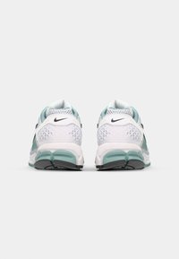 Bijele i akvamarin Nike tenisice s mrežastim materijalom, teksturiranim pete i crnim logotipom. Sadrže podložene potplate i zakrivljen dizajn.