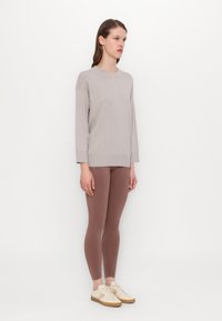 Lys grå strikkegenser med et teksturert rutenettmønster, brukt med støvete rosafargede leggings og kremfargede sneakers med lysebrune såler.
