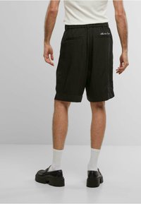 Svarte shorts med en løs passform, elastisk midje, sidelommer, og en subtil logo-detalj. Båret med hvite sokker og platå sko.