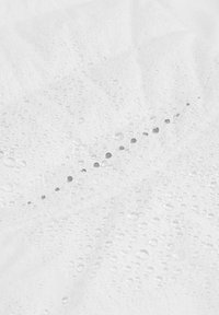 Surface en tissu blanc avec des gouttes d'eau visibles, mettant en avant une texture lisse et un éclat subtil, présentant une apparence froissée.