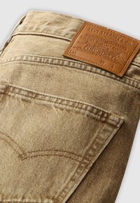 Beige denim jeans gevouwen, met de achterkant zichtbaar en een bruine leren merklabel van Levi Strauss & Co. gestikt boven de achterzak.