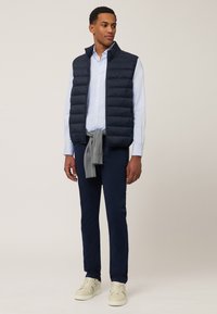 Mornarska jakna s kvadratima preko svijetloplave košulje, sivi pulover vezan oko struka i mornarske hlače. Krem tenisice upotpunjuju izgled.