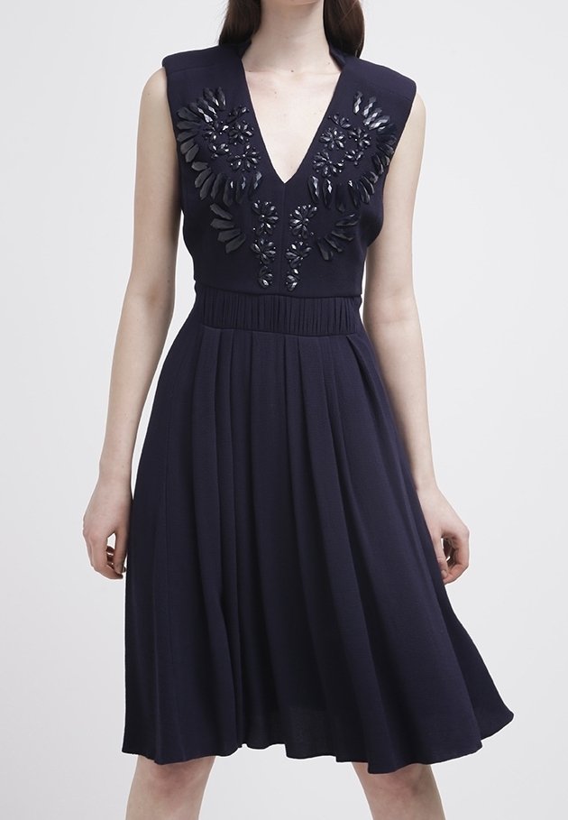 Marinblå klänning med djup V-ringning och ärmlös design, prydd med blommig broderi och paljetter på överdelen, utsvängd kjol, mjukt tyg.