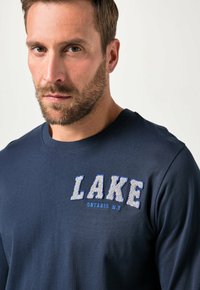 Marinblå långärmad t-shirt i bomull med texturerad brodyr av "LAKE" i vitt och blått, med "ONTARIO N.Y." under.