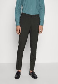 Dunkelgrüne, taillierte Hose in Slim-Fit, mit glatter Textur, geradem Bund mit Knopfverschluss, kombiniert mit schwarzen Slippern und einem türkisfarbenen Hemd.