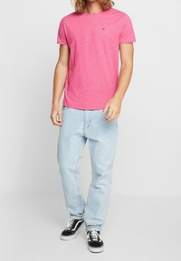 Růžové tričko s krátkým rukávem a kulatým výstřihem, kombinované s volnými světle modrými džíny a černobílými teniskami.