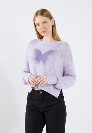 Pull en tricot lilas avec une coupe ample et des poignets côtelés. Présente un motif de papillon en lilas plus foncé au centre. Assorti à un jean noir taille haute.