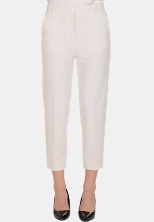 Pantaloni su misura color crema, tagliati, con tasche frontali e chiusura a bottone, indossati con tacchi neri a punta.