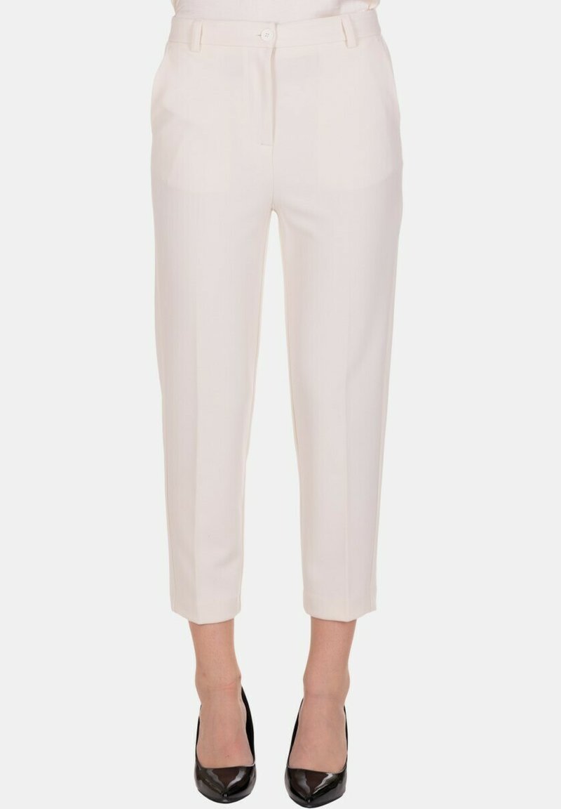 Pantaloni su misura color crema, tagliati, con tasche frontali e chiusura a bottone, indossati con tacchi neri a punta.