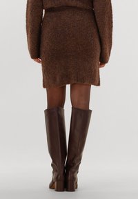 Bruine, zacht gebreide trui met bijpassende aansluitende rok en bruine leren laarzen tot de knie met dikke hakken, gezien van achteren.