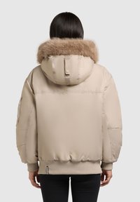 Beige pufferjacka med foder av pälskantad huva, ribbade muddar och nederkant. Slät textur, oversized passform och sidofickor synliga i designen.