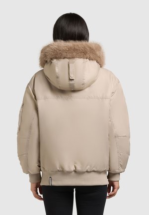 Giacca puffa beige con cappuccio foderato in pelliccia, polsini e orlo a costine. Tessuto morbido, vestibilità over size e tasche laterali visibili nel design.